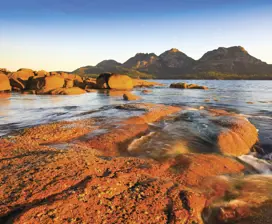 View of the The Hazards in Coles Bay. The rocks shine red as the sun sets over the blue lake.  
