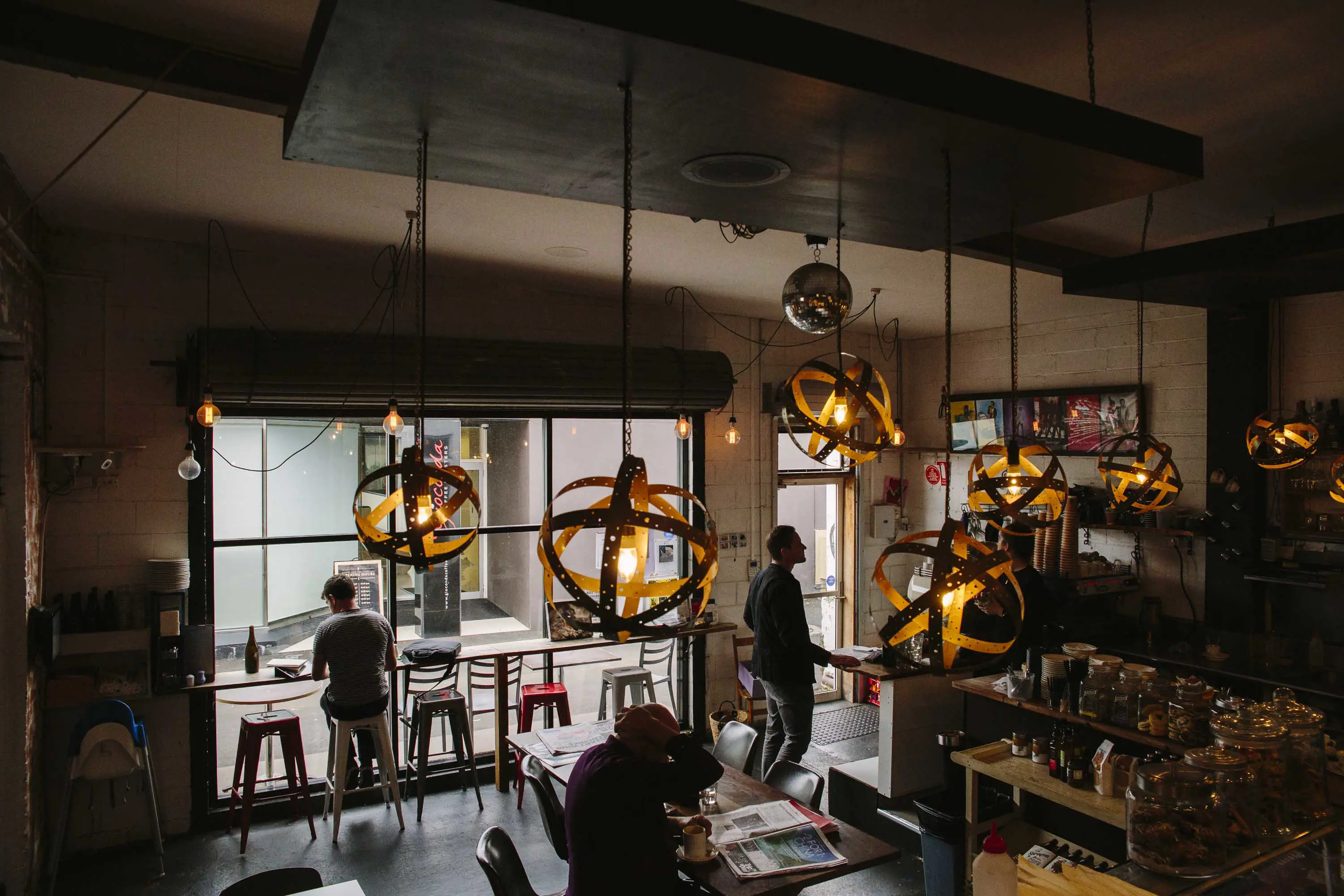 People sit inside the tall windows of a cafe, decorated with large circular lights, hung from the ceiling.
